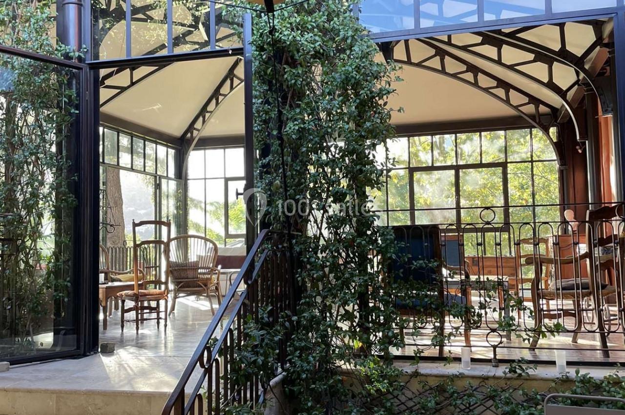 Verrière lumineuse avec plantes grimpantes, mobilier en bois et métal, et escaliers menant à une terrasse intérieure.