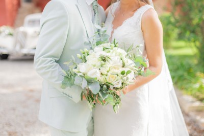 Main d'une personne tenant légèrement une robe blanche, avec un bracelet fin et une bague visible.