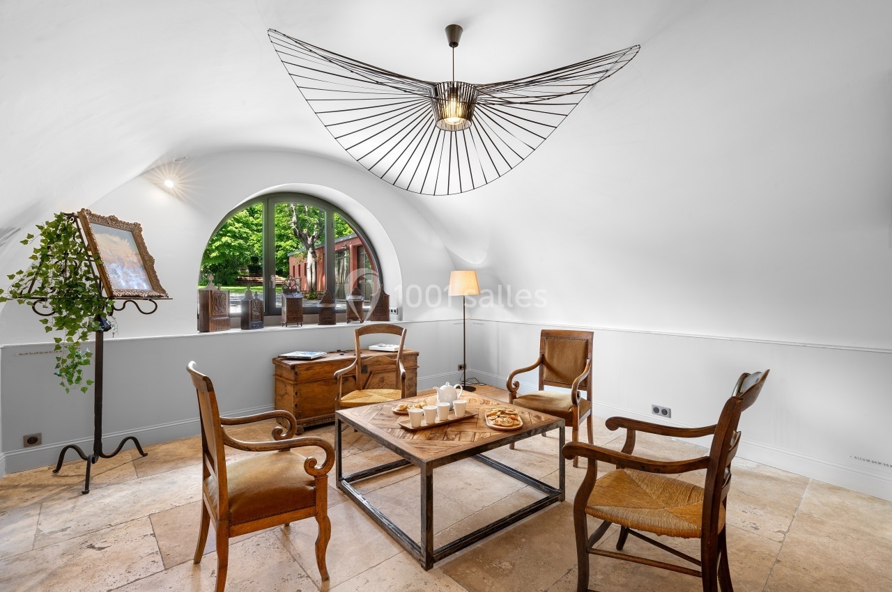 Salle lumineuse avec table basse en bois, quatre chaises, une lampe design et une grande fenêtre en arche donnant sur un…
