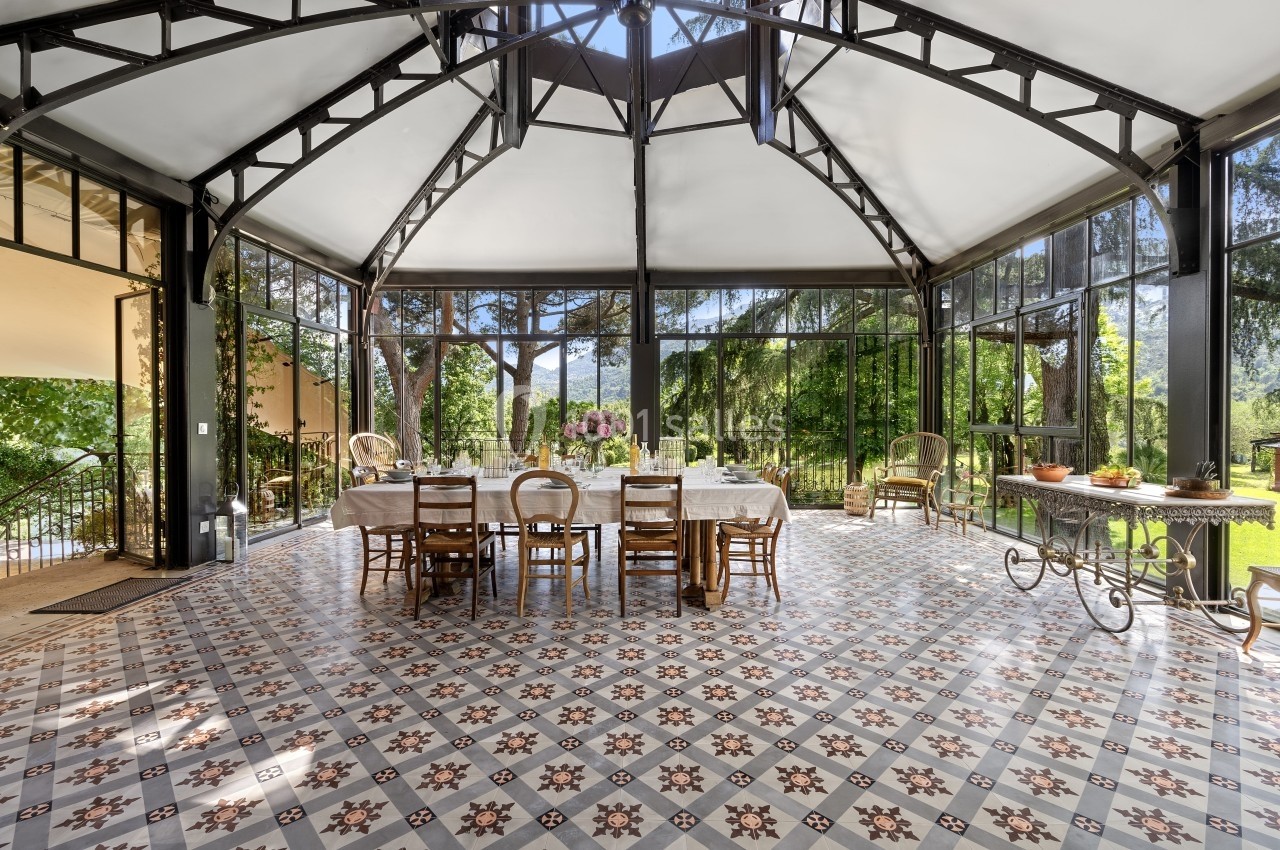 Salle à manger lumineuse avec grandes baies vitrées, carrelage à motifs et table dressée au centre.
