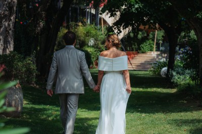 Main d'une personne tenant légèrement une robe blanche, avec un bracelet fin et une bague visible.