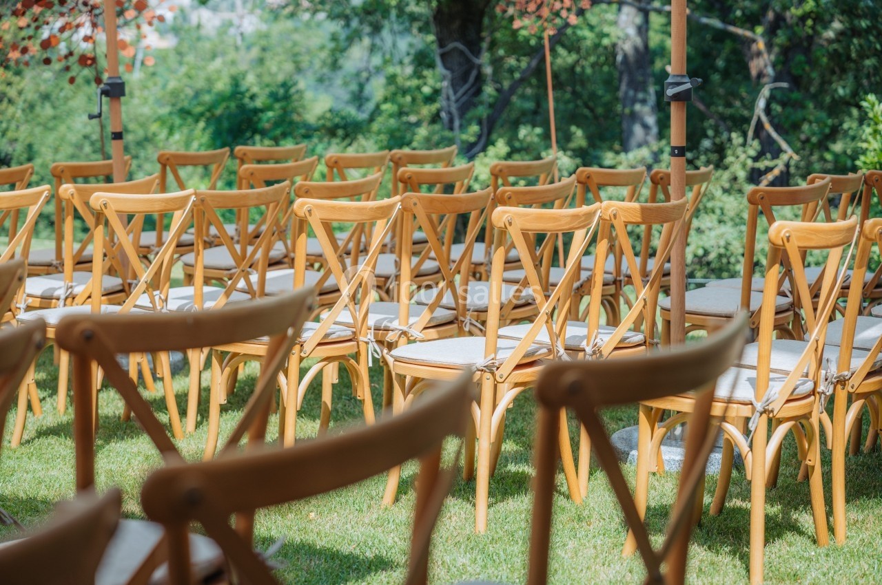 Chaises en bois alignées sur une pelouse, disposées pour un événement en extérieur sous un ciel ensoleillé.