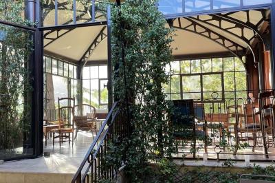 Bâtiment aux murs rouges avec de grandes baies vitrées, entouré d'arbres et d'une fontaine en arrière-plan.