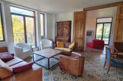 Bâtiment aux murs rouges avec de grandes baies vitrées, entouré d'arbres et d'une fontaine en arrière-plan.