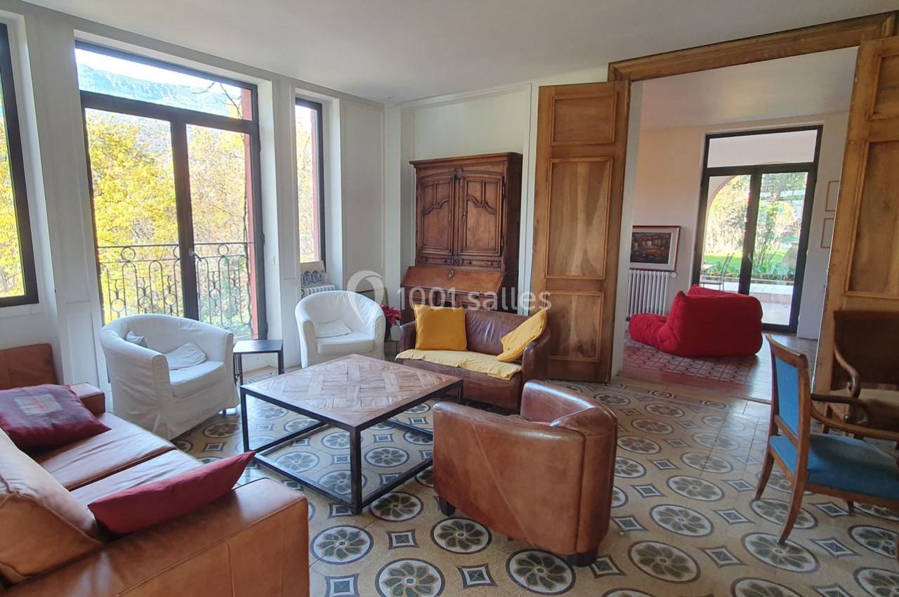 Salon lumineux avec canapés, fauteuils en cuir, table basse en bois, sol en carreaux décoratifs et grandes fenêtres.