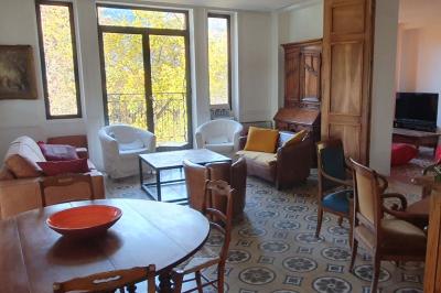 Bâtiment aux murs rouges avec de grandes baies vitrées, entouré d'arbres et d'une fontaine en arrière-plan.