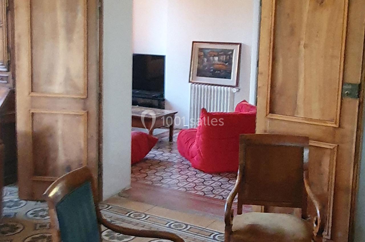 Une pièce avec des fauteuils, une télévision, un tapis à motifs et des portes en bois ouvertes.