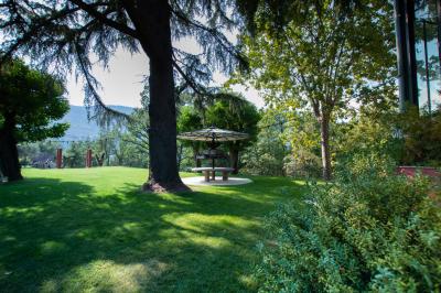 Bâtiment aux murs rouges avec de grandes baies vitrées, entouré d'arbres et d'une fontaine en arrière-plan.