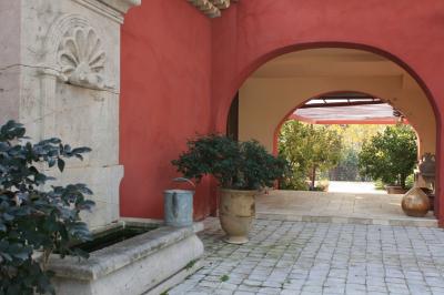 Bâtiment aux murs rouges avec de grandes baies vitrées, entouré d'arbres et d'une fontaine en arrière-plan.