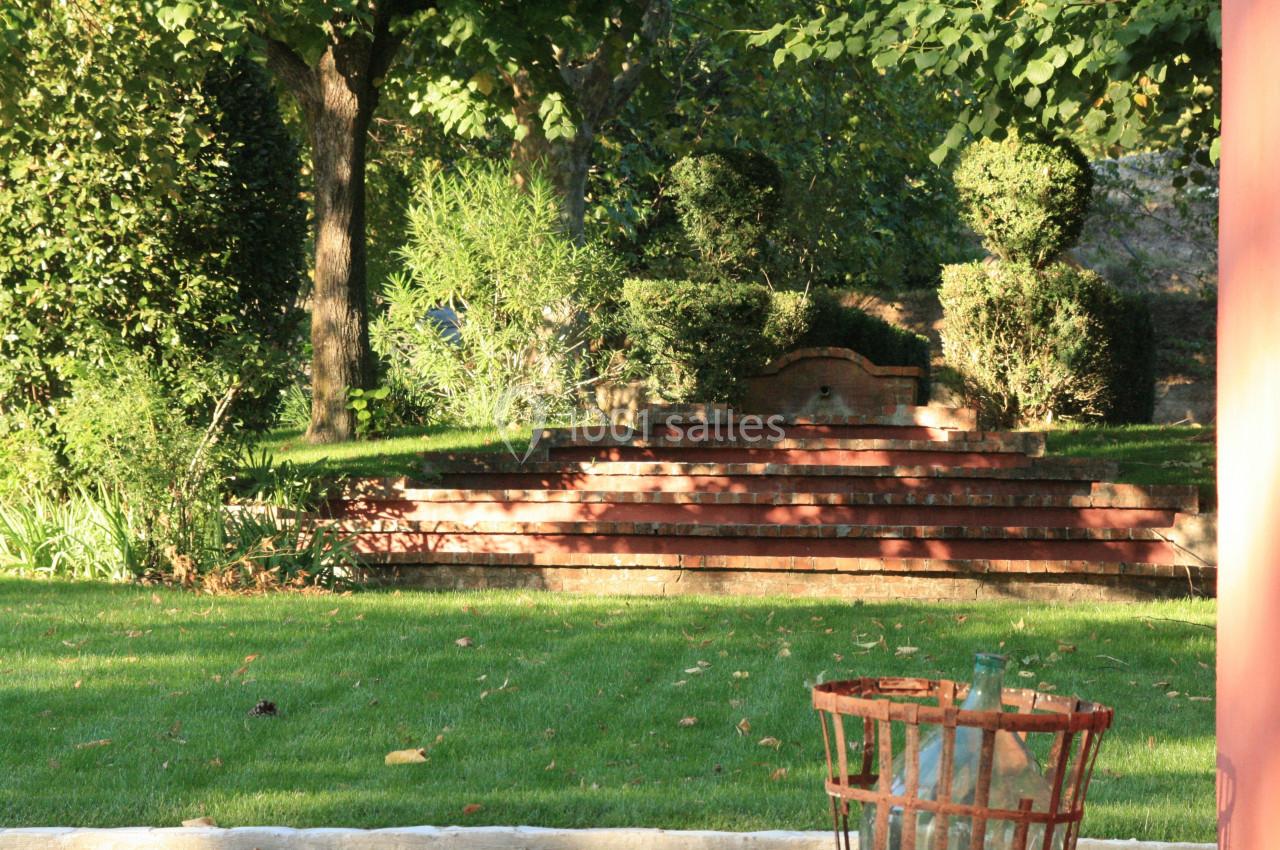 Escalier en briques rouges entouré de verdure dans un jardin, avec une corbeille en métal au premier plan.