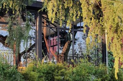 Bâtiment aux murs rouges avec de grandes baies vitrées, entouré d'arbres et d'une fontaine en arrière-plan.