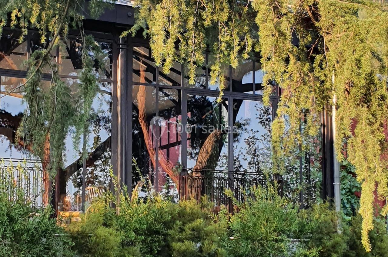 Façade d'un bâtiment entouré de végétation, avec des arbres et un jardin verdoyant au premier plan.