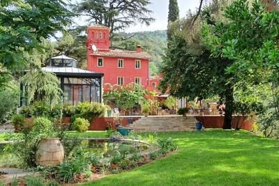 Bâtiment aux murs rouges avec de grandes baies vitrées, entouré d'arbres et d'une fontaine en arrière-plan.