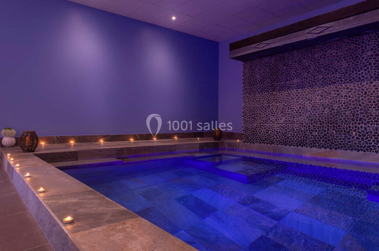 Piscine intérieure éclairée par des bougies, avec un mur en pierres sombres et une ambiance tamisée.