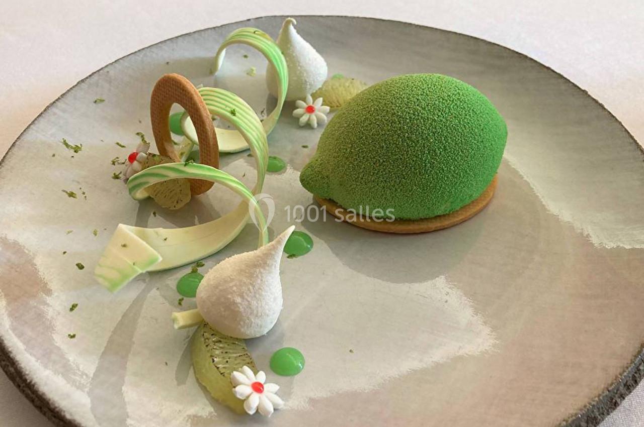 Dessert raffiné en forme de citron vert avec décorations sucrées, meringues et touches de crème sur une assiette.