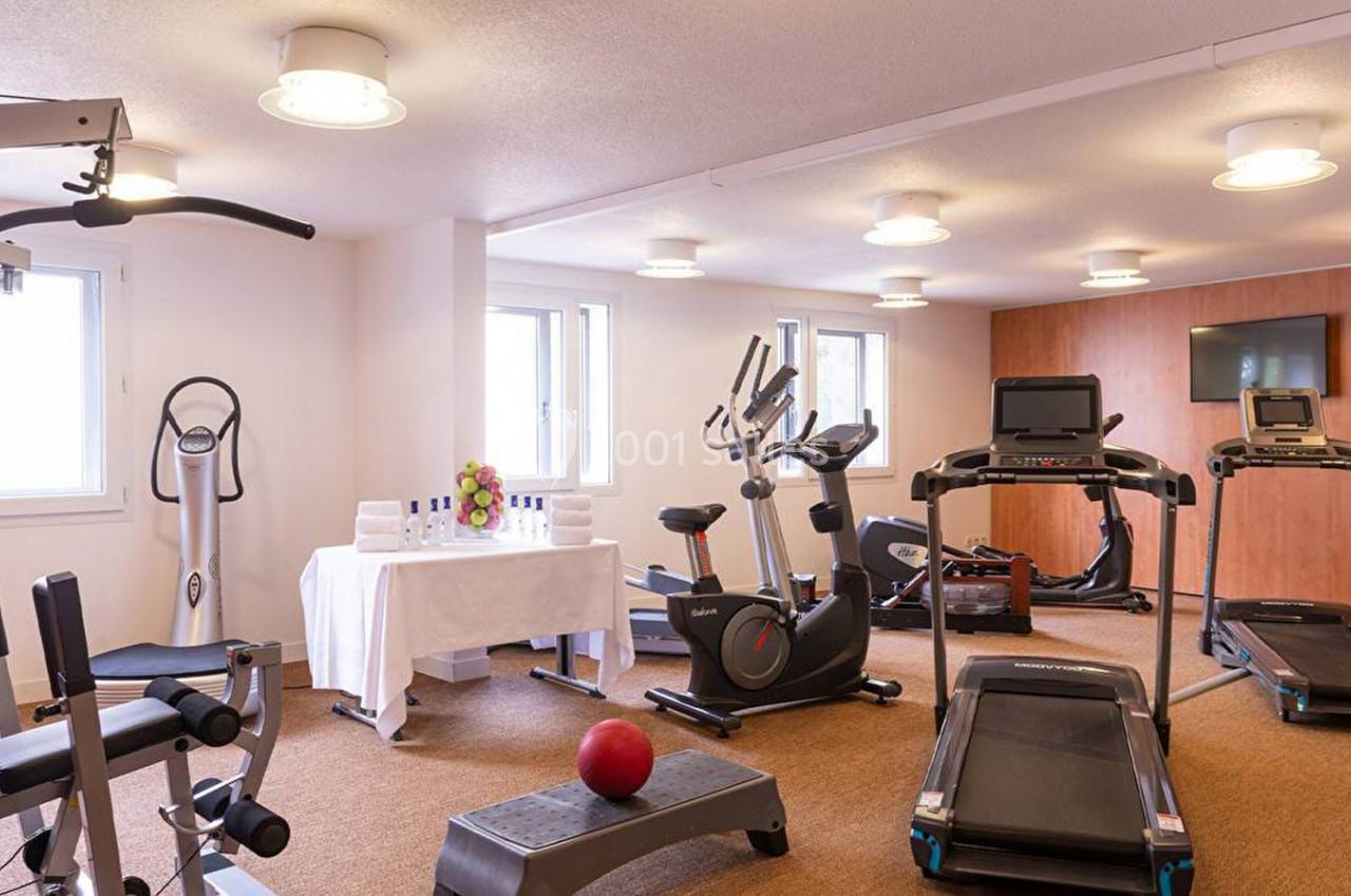 Salle de sport équipée de tapis de course, vélos d'exercice, appareils de musculation et table avec serviettes.