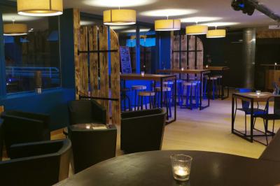 Salle moderne avec tables hautes en bois, chaises en métal, éclairage chaleureux et grandes fenêtres avec stores.