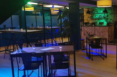 Salle moderne avec tables hautes en bois, chaises en métal, éclairage chaleureux et grandes fenêtres avec stores.