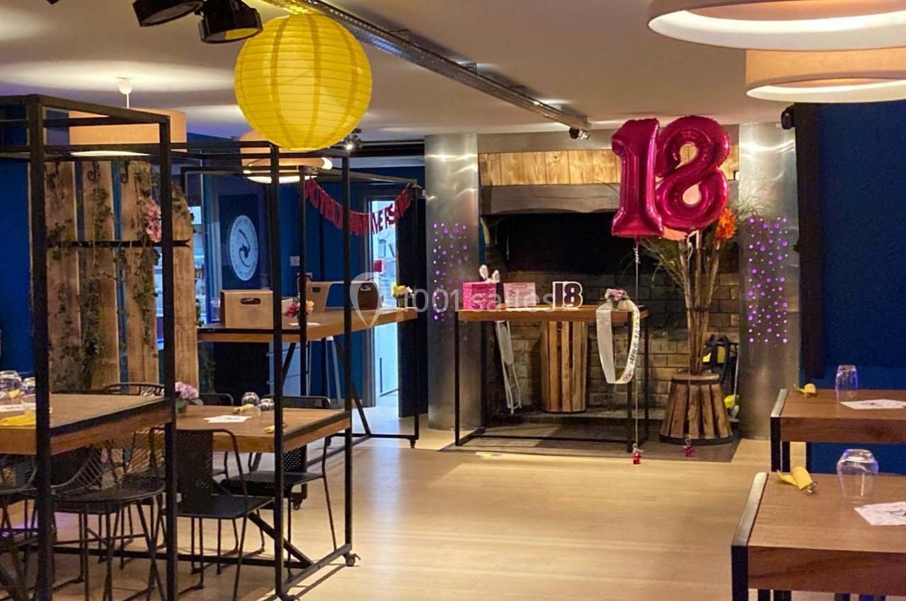 Salle décorée pour un 18e anniversaire, avec ballons roses, guirlandes et tables dressées dans un cadre chaleureux.