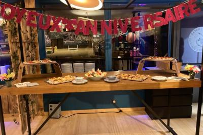 Salle moderne avec tables hautes en bois, chaises en métal, éclairage chaleureux et grandes fenêtres avec stores.