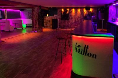 Salle moderne avec tables hautes en bois, chaises en métal, éclairage chaleureux et grandes fenêtres avec stores.