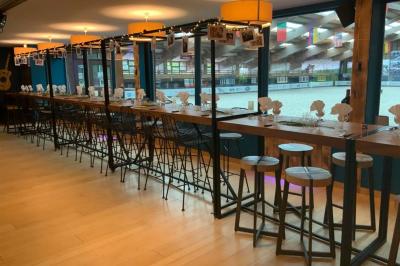 Salle moderne avec tables hautes en bois, chaises en métal, éclairage chaleureux et grandes fenêtres avec stores.