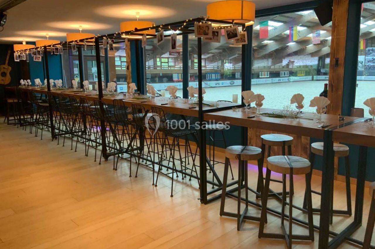 Salle aménagée avec de longues tables en bois, chaises hautes et vue sur une carrière équestre à travers des baies vitrées.