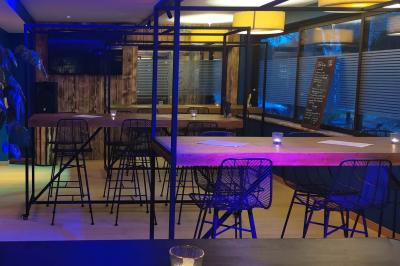 Salle moderne avec tables hautes en bois, chaises en métal, éclairage chaleureux et grandes fenêtres avec stores.