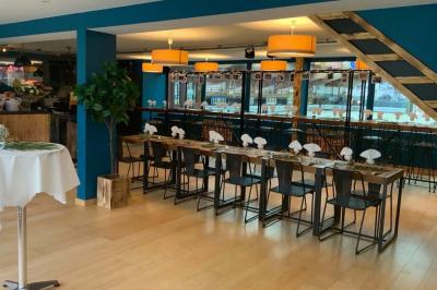 Salle moderne avec tables hautes en bois, chaises en métal, éclairage chaleureux et grandes fenêtres avec stores.