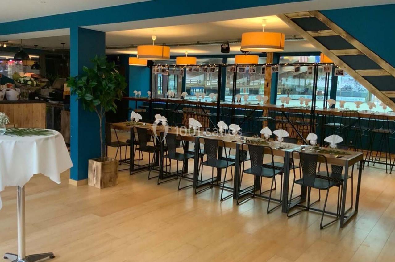 Salle lumineuse avec tables dressées, chaises noires, décor moderne, plantes et éclairage suspendu.