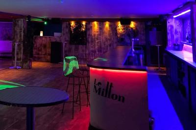 Salle moderne avec tables hautes en bois, chaises en métal, éclairage chaleureux et grandes fenêtres avec stores.