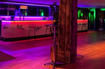 Salle moderne avec tables hautes en bois, chaises en métal, éclairage chaleureux et grandes fenêtres avec stores.