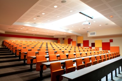 Salle de conférence moderne avec des rangées de sièges orange et un projecteur suspendu au plafond.