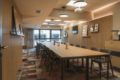 Salle de conférence moderne avec des rangées de sièges orange et un projecteur suspendu au plafond.