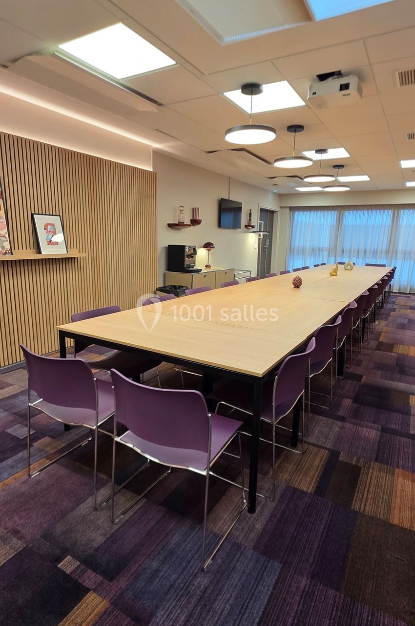 Salle de réunion avec une longue table en bois, chaises violettes, éclairage suspendu et décorations murales.