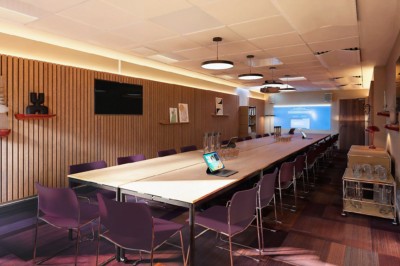 Salle de conférence moderne avec des rangées de sièges orange et un projecteur suspendu au plafond.