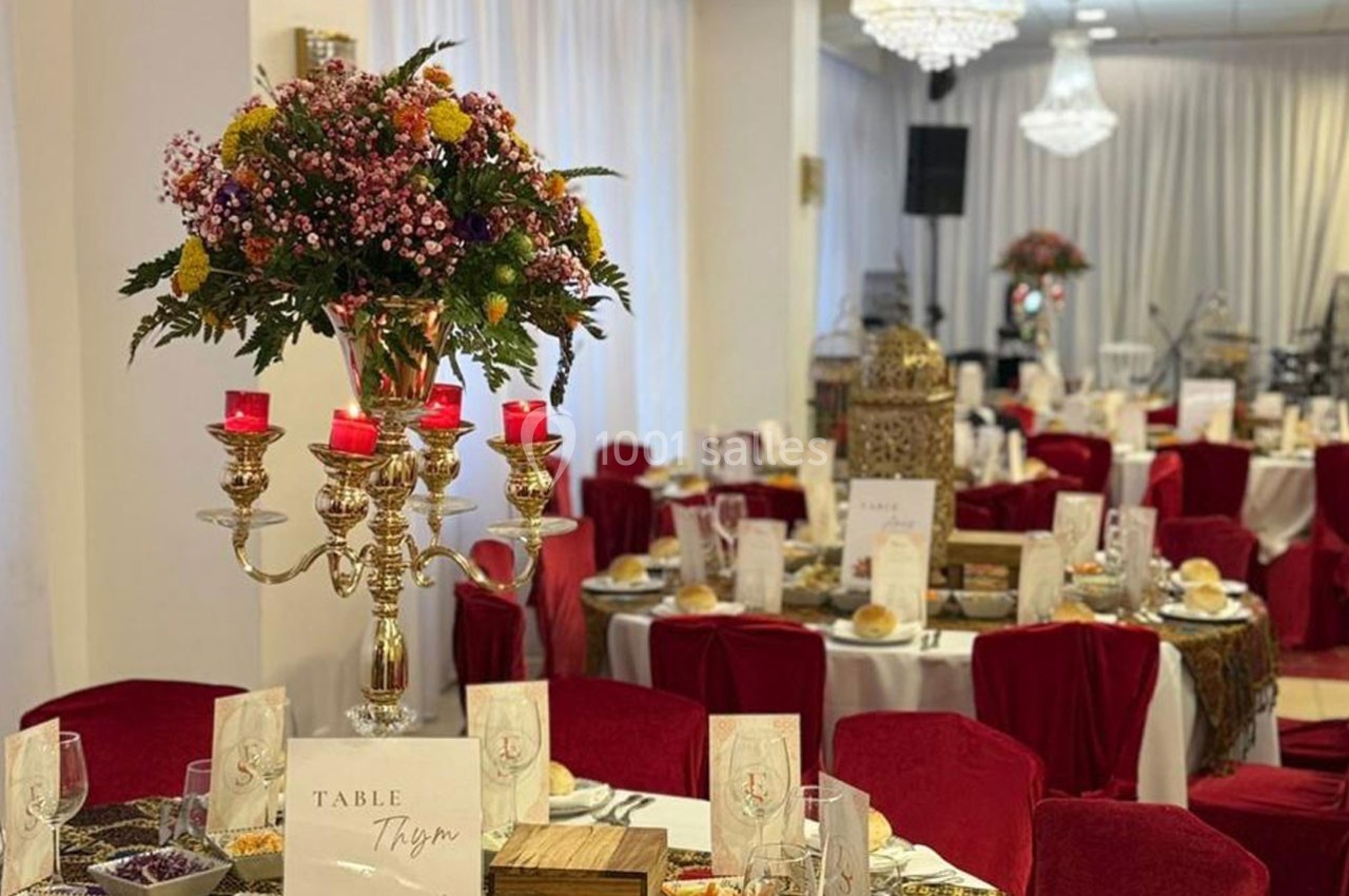 Salle de réception décorée avec des chandeliers, des fleurs colorées et des tables dressées pour un événement.