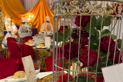 Des roses rouges dans une cage décorative dorée, entourées de tables ornées pour un événement festif.
