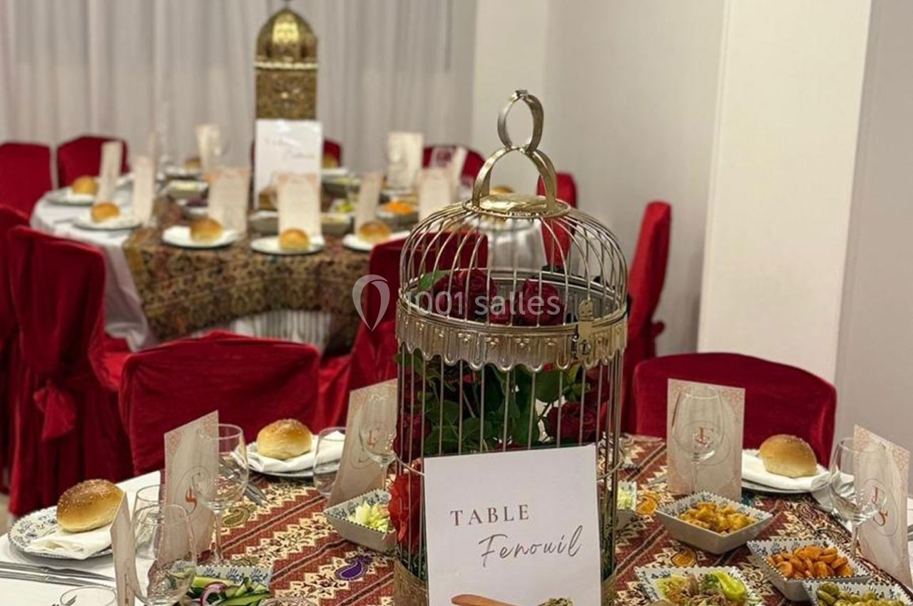 Table décorée avec une nappe ornée, des chaises rouges, une cage dorée au centre et des plats variés disposés autour.