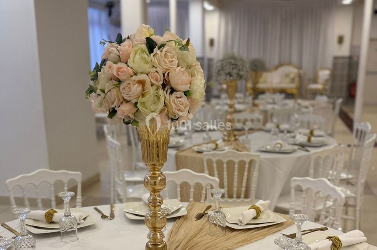 Salle de réception élégante avec tables dressées, décorations florales et chaises blanches.