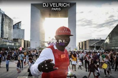 Un DJ mixe en plein air devant une foule, avec l'Arche de la Défense en arrière-plan.