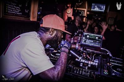 Un DJ mixe en plein air devant une foule, avec l'Arche de la Défense en arrière-plan.