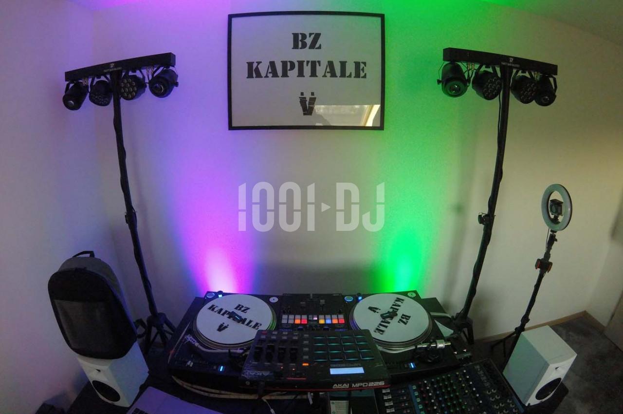 Équipement de DJ avec platines, table de mixage et éclairages colorés dans une pièce décorée sobrement.