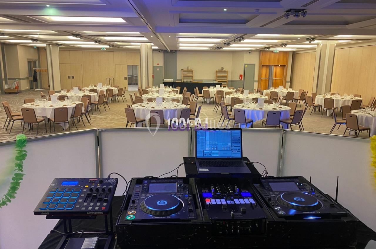 Console de DJ avec platines et ordinateur portable, vue sur une salle de réception aménagée avec des tables rondes dressées.