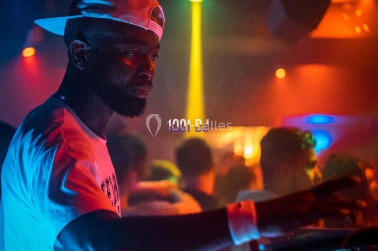 Un DJ mixant sur une console dans une ambiance de boîte de nuit avec éclairages colorés.