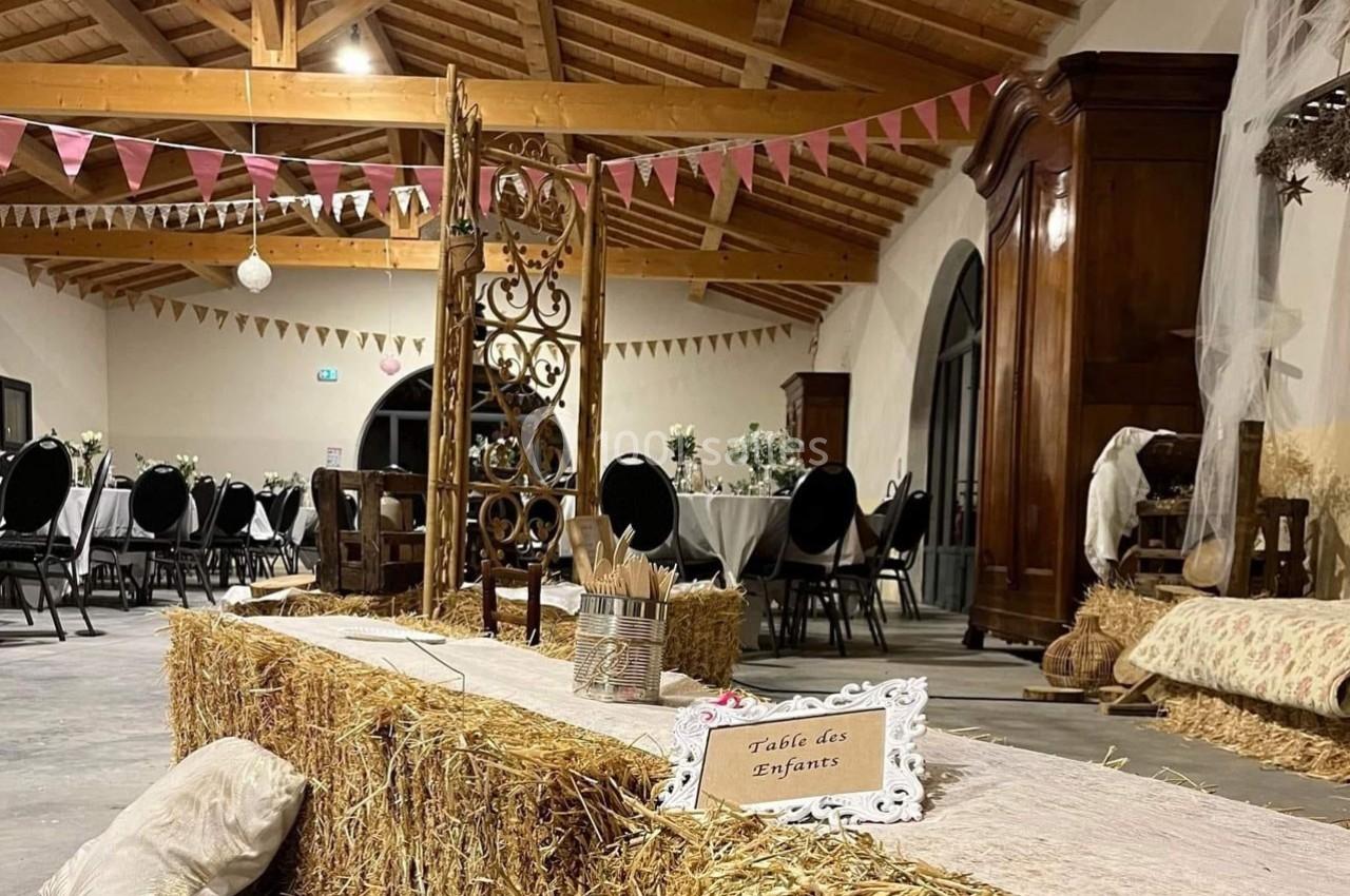 Salle décorée pour un événement avec des tables rondes, des bottes de paille et une pancarte ’Table des Enfants’.