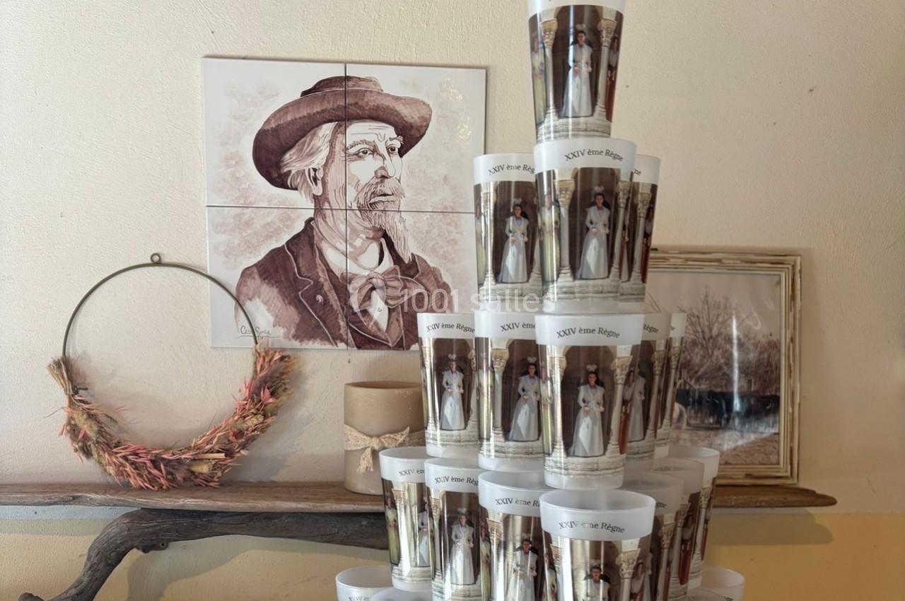 Bougies décoratives empilées devant des illustrations murales, dont un portrait ancien et une couronne en branches sèches.