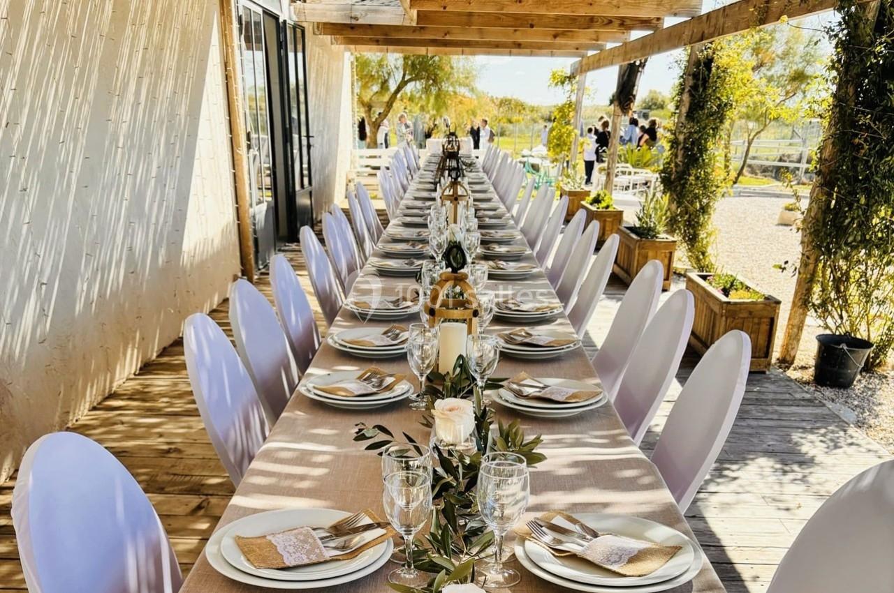 Grande table extérieure décorée pour un événement, avec nappes beige, vaisselle élégante et centre de table floral.