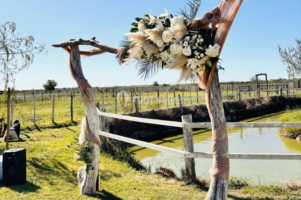 Arche en bois décorée de fleurs blanches et feuillages, installée près d'un étang dans un cadre champêtre.