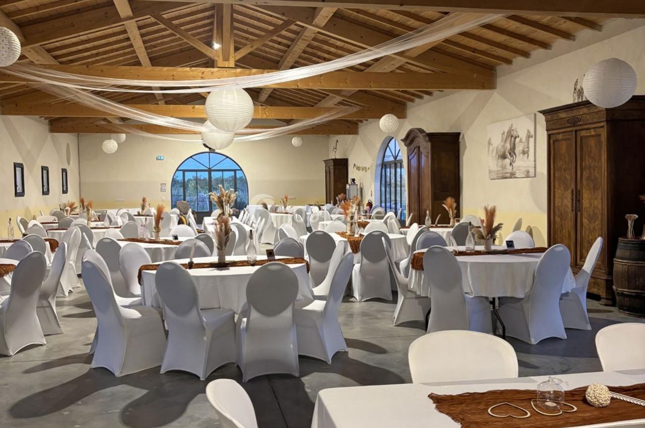 Salle de réception décorée avec des tables rondes et rectangulaires, nappes blanches et éléments rustiques.